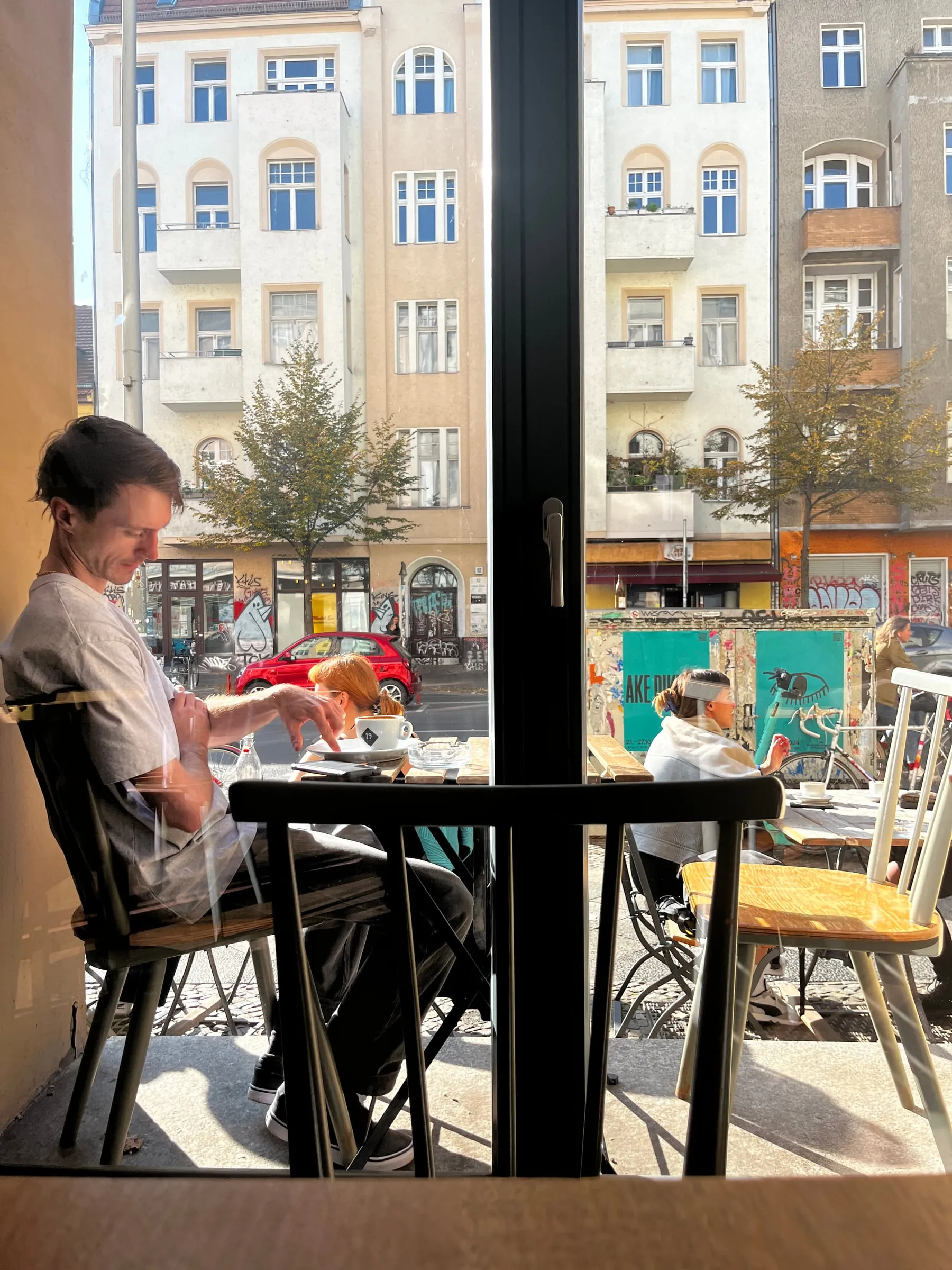 A person seated at a cafe table beside a tall window overlooking the street.