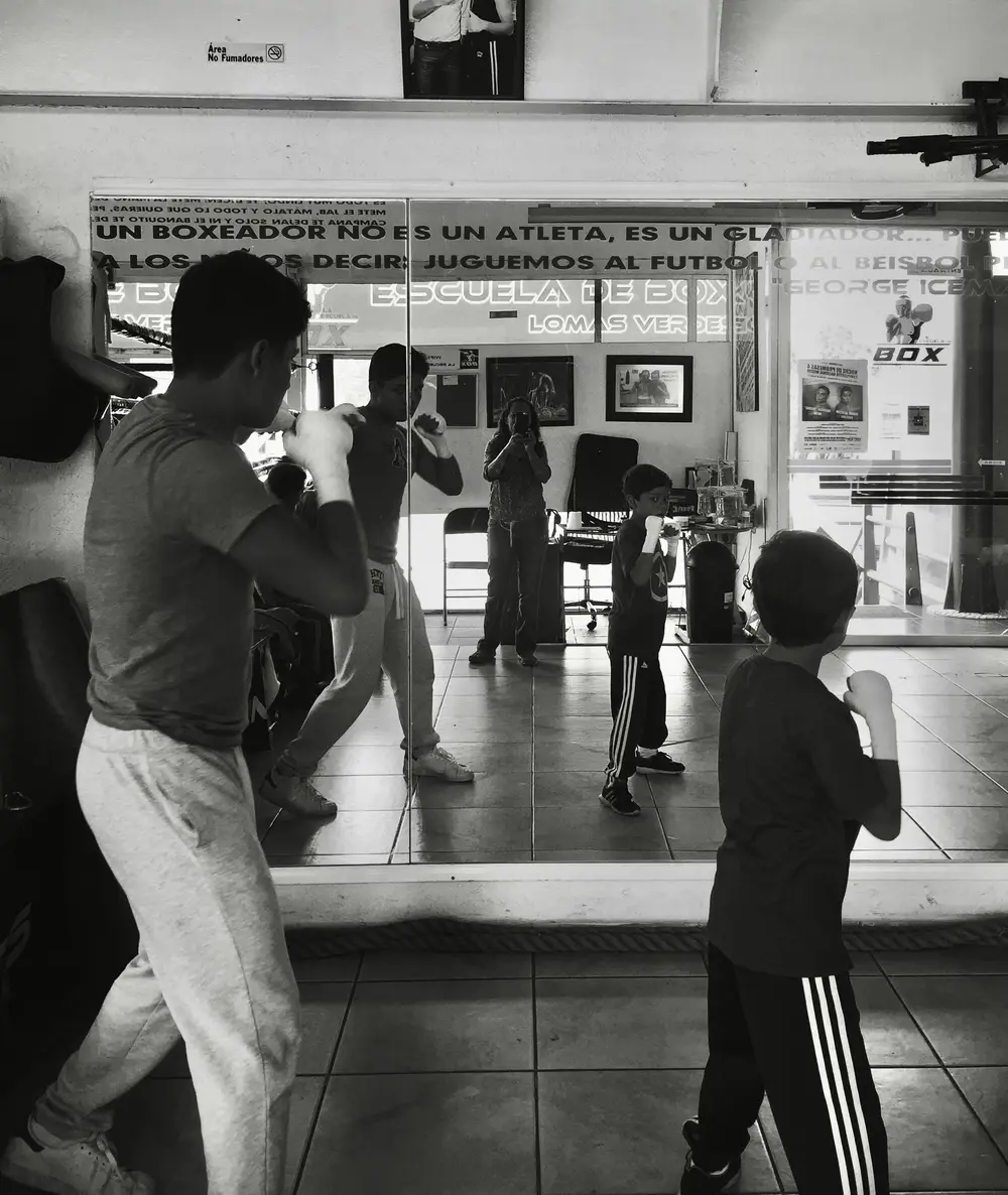 Two people practicing boxing in front of a wall mirror, photographed in black and white.