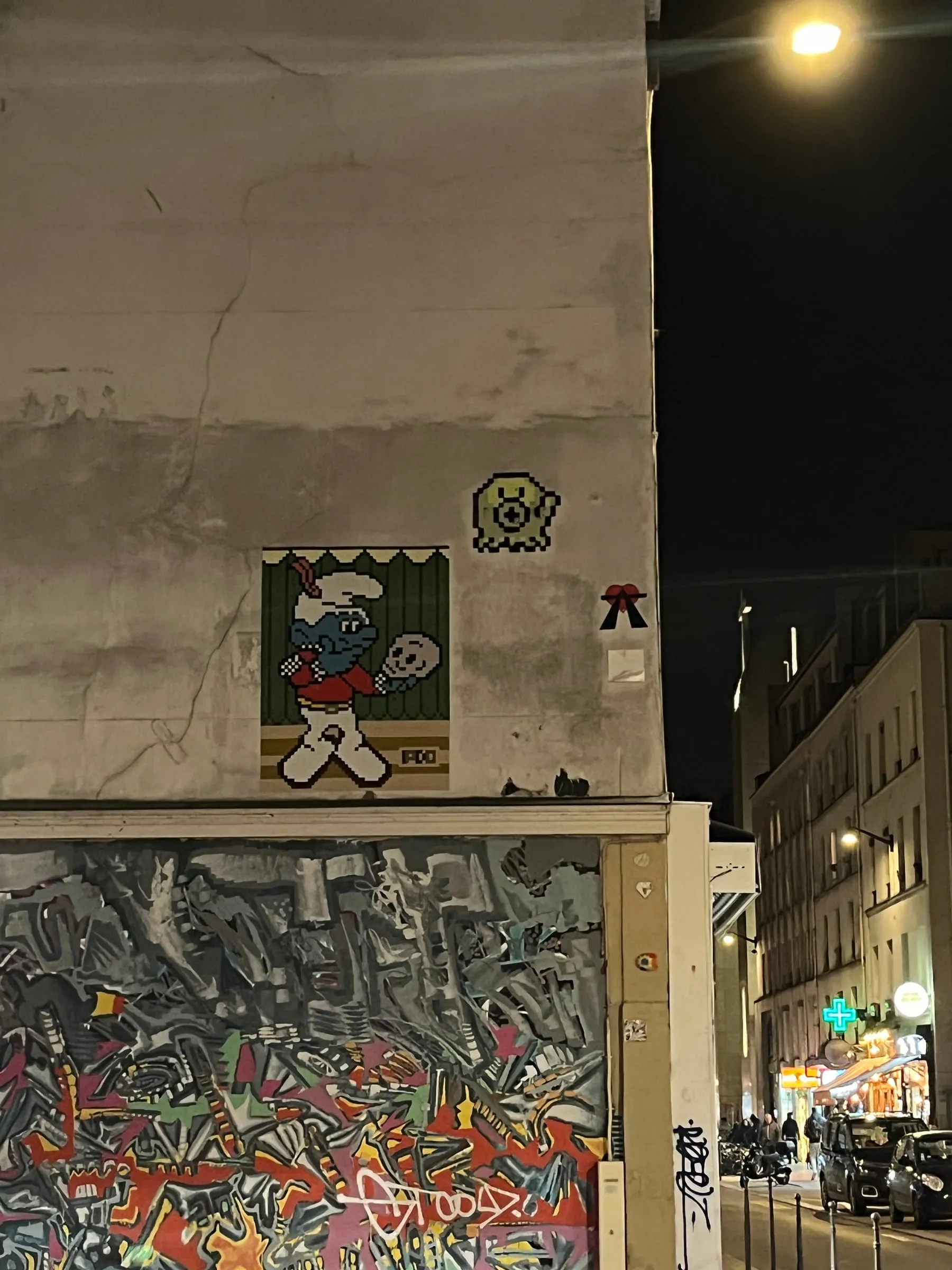 Graffiti and a small pixel-art figure on the corner of a building at night.