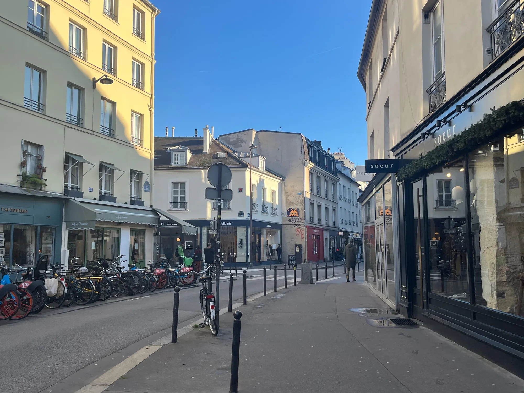 A narrow street lined with pale apartment buildings, bicycles and short bollards.