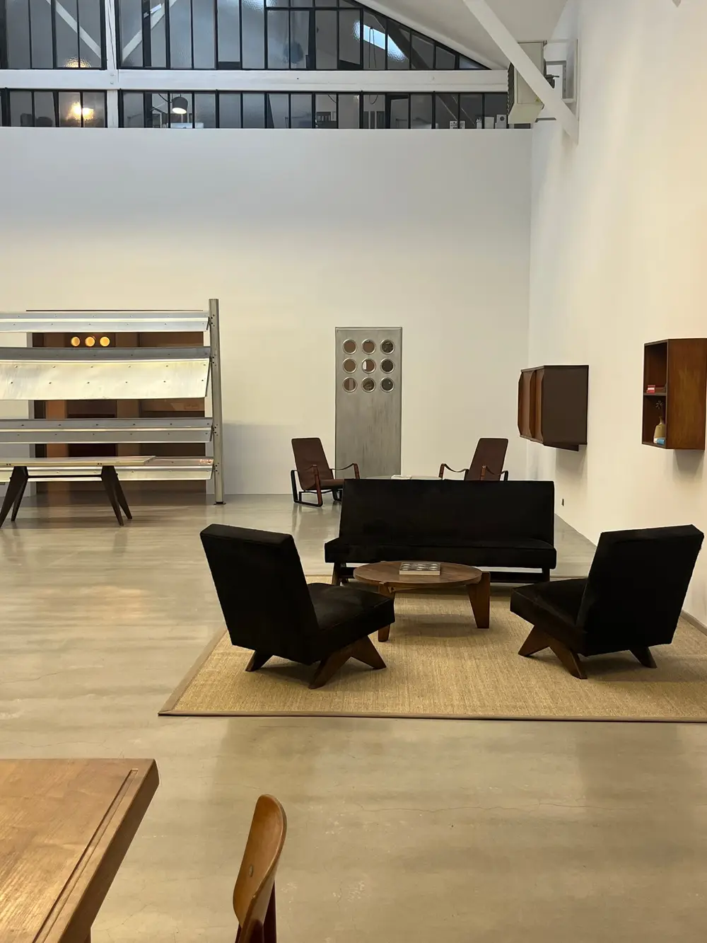 Dark chairs and a low table arranged inside a bright, high-ceilinged gallery.