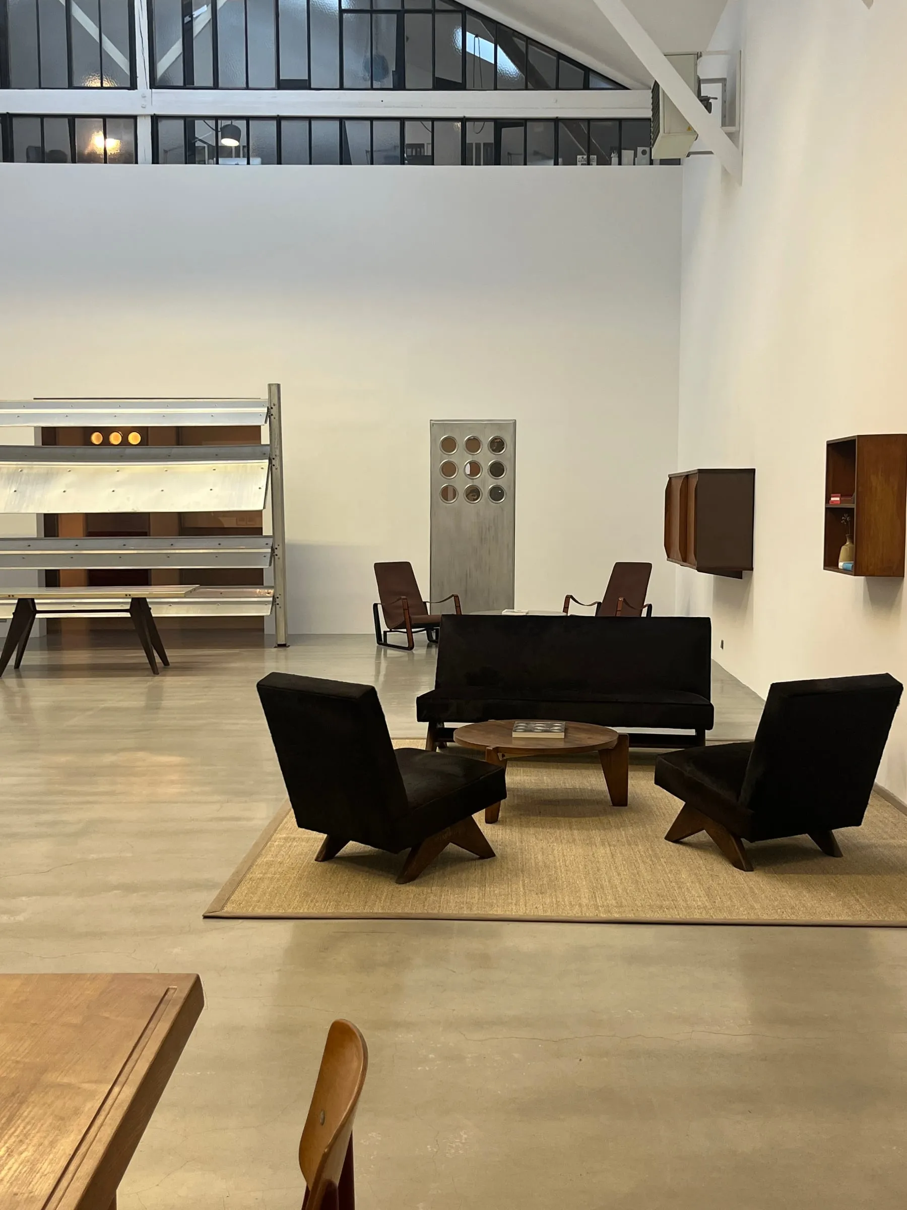 Dark chairs and a low table arranged inside a bright, high-ceilinged gallery.