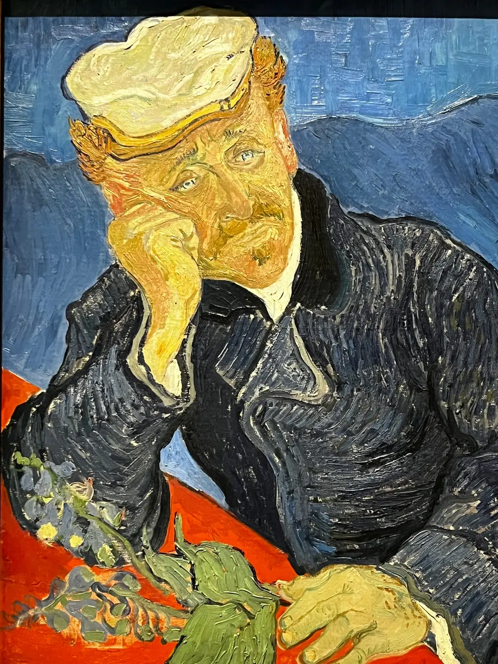 A painting of a man resting his head on one hand beside flowers and books.