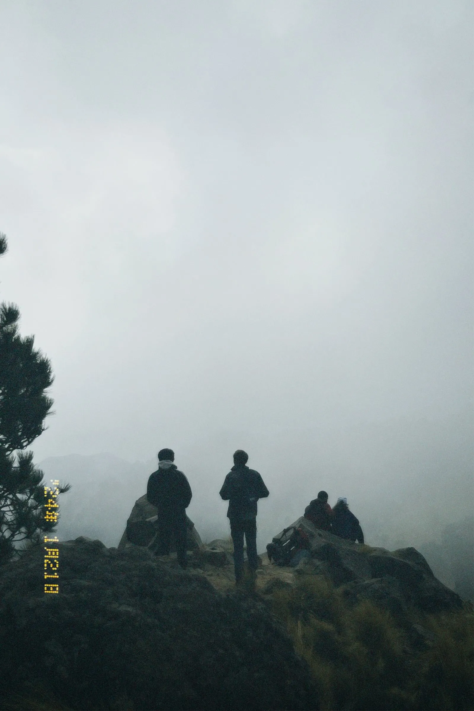 Hikers silhouetted on a rocky ridge surrounded by fog.