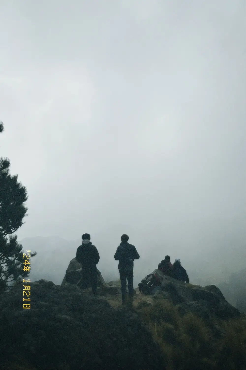 Hikers silhouetted on a rocky ridge surrounded by fog.