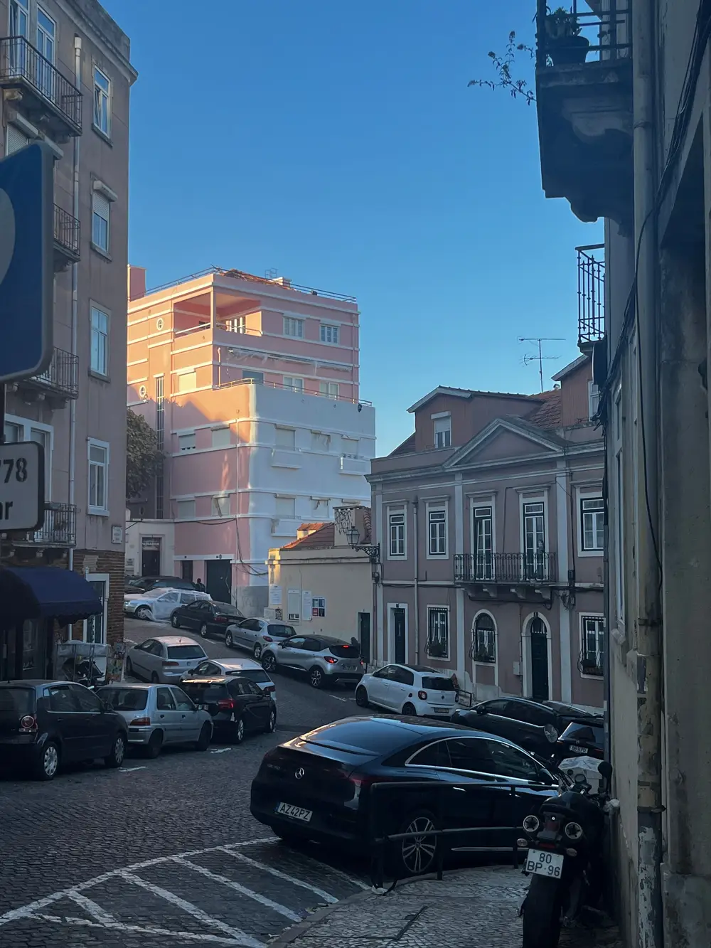 Parked cars on a sloping street between colorful buildings in Lisbon.