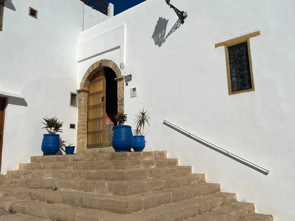 Stone steps leading to an arched wooden door, with blue plant pots against white walls.