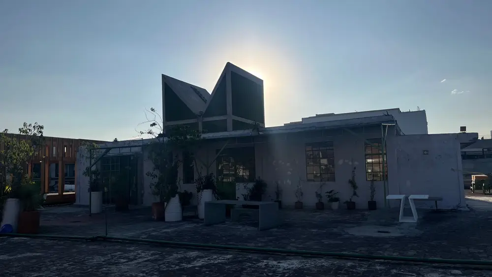 A low concrete building with angular rooftop structures silhouetted against the sun.