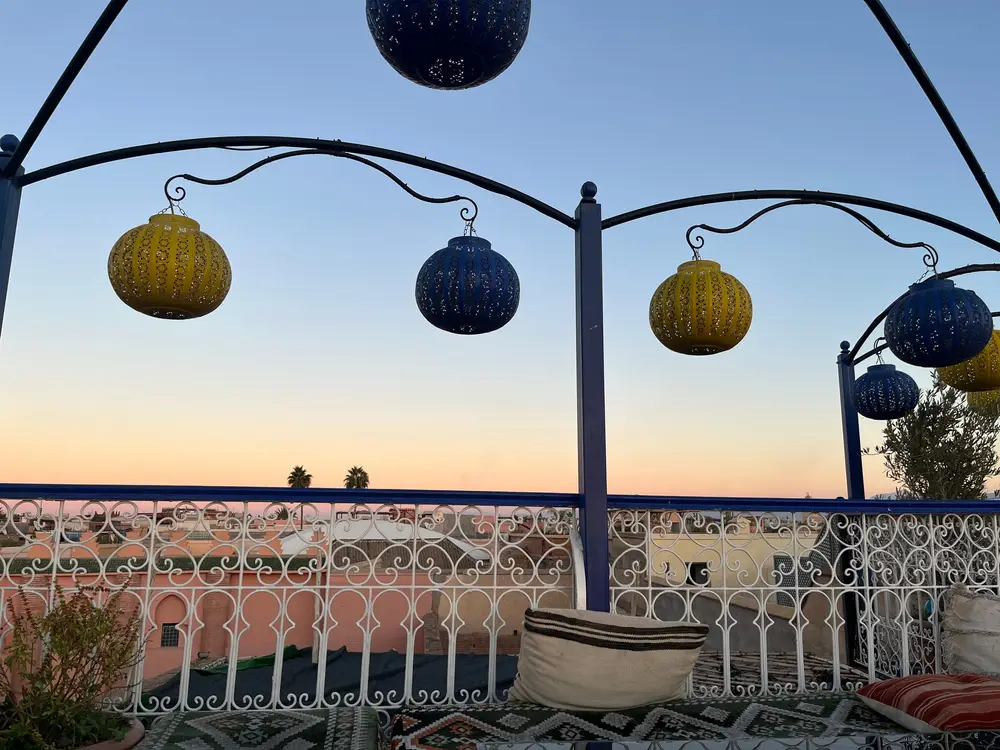 Blue and yellow lanterns hanging above a rooftop terrace at sunset.