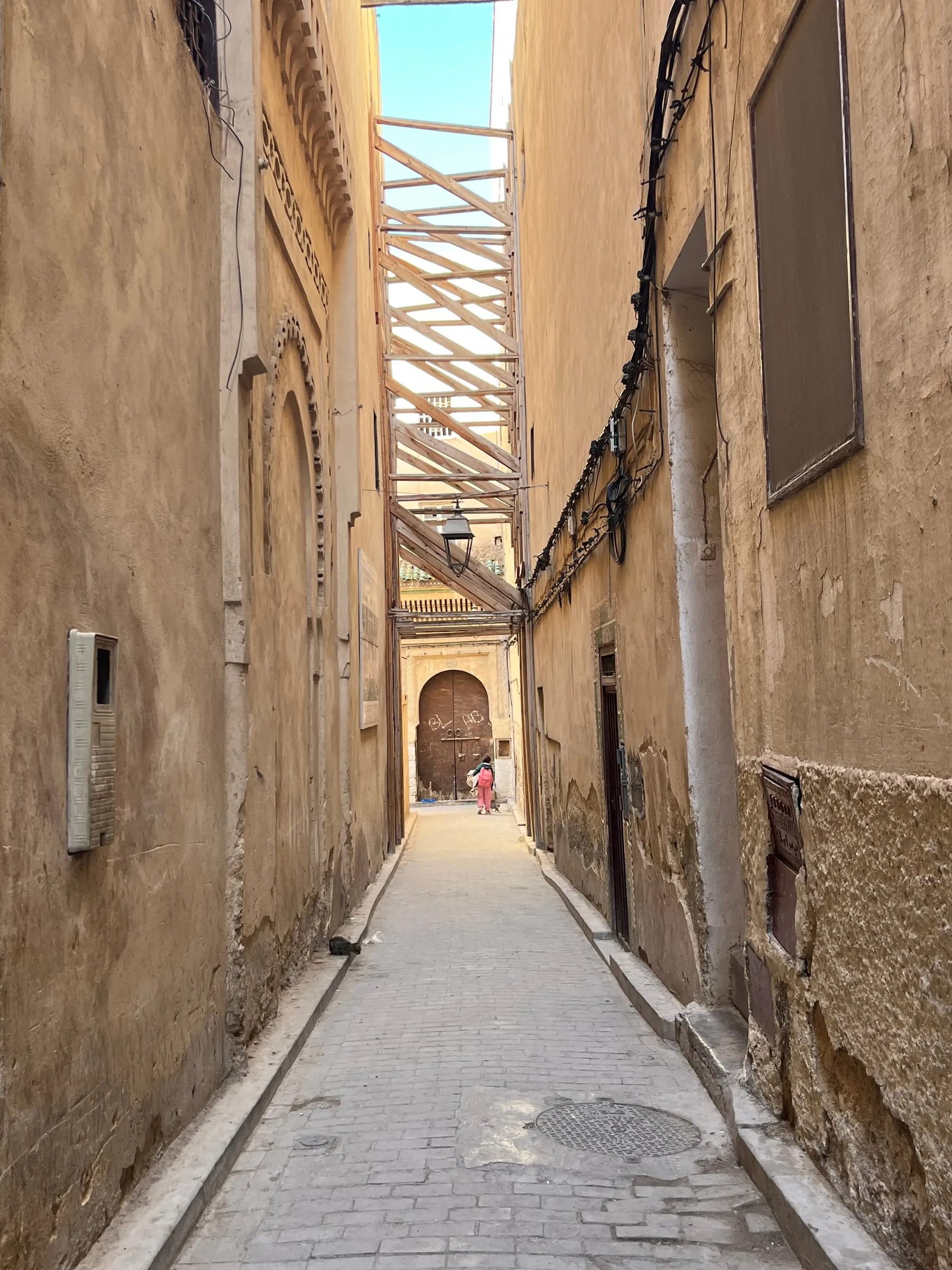 A narrow alley between tall ochre walls, with wooden beams overhead.