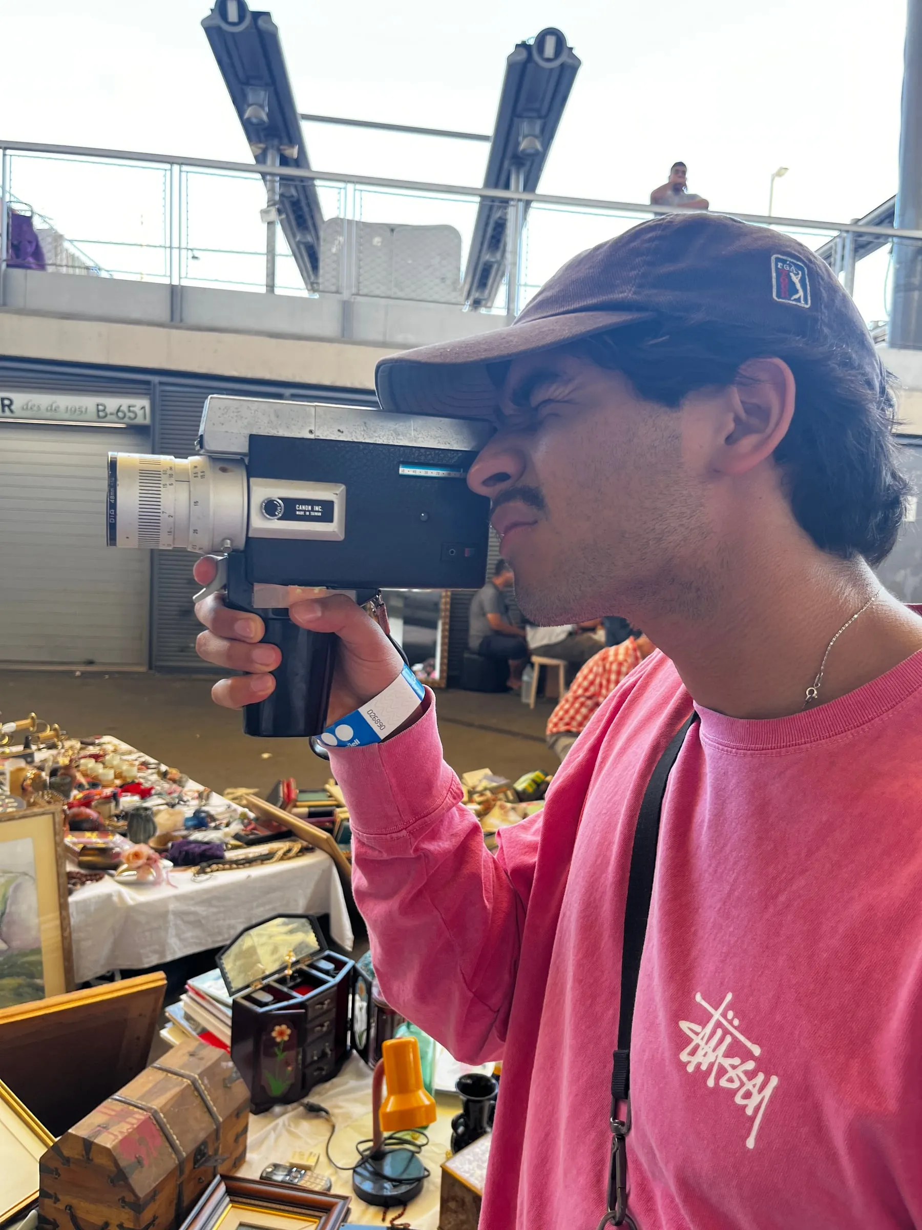 A person in a pink shirt holding a small video camera inside a market.