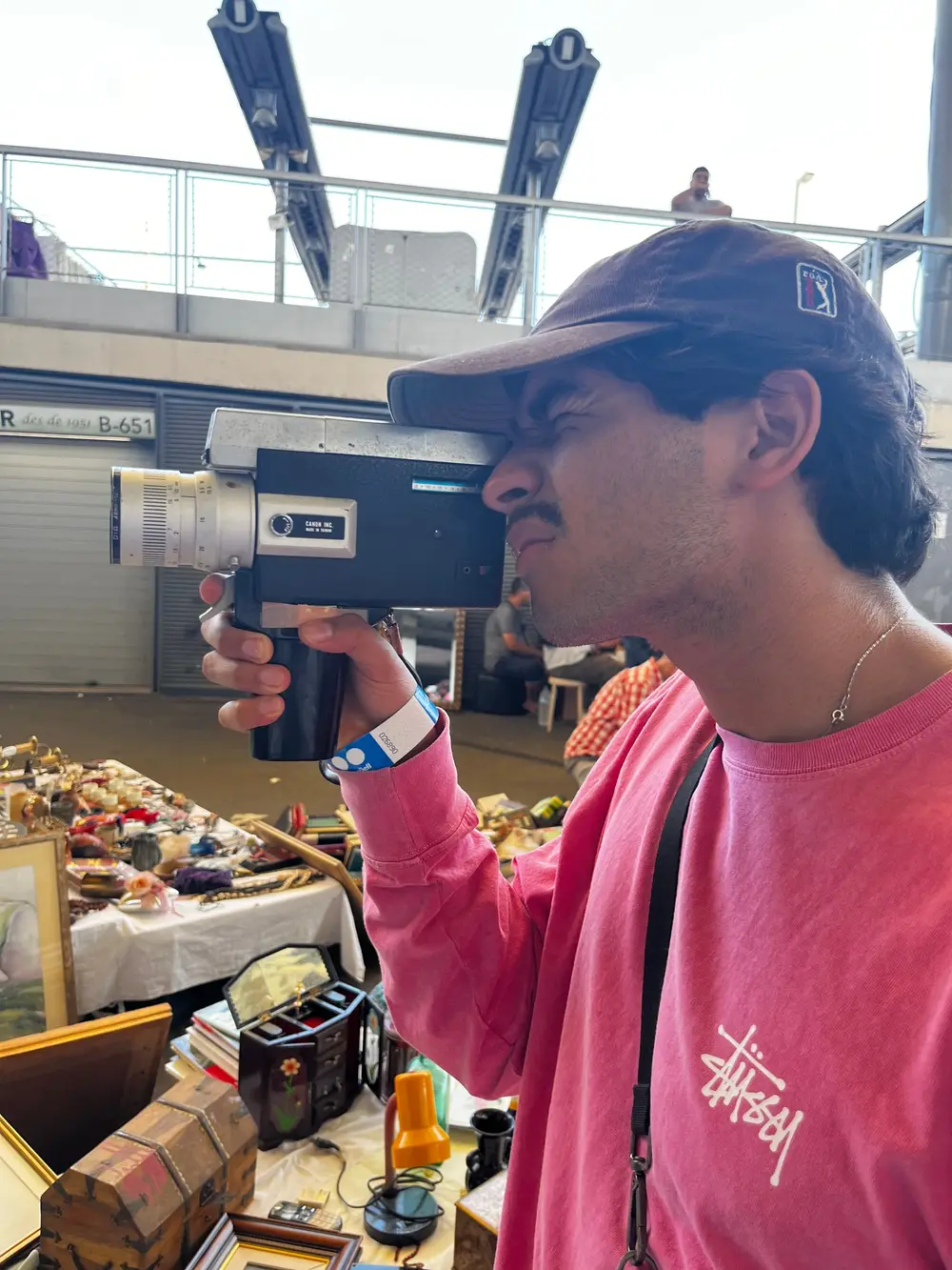 A person in a pink shirt holding a small video camera inside a market.