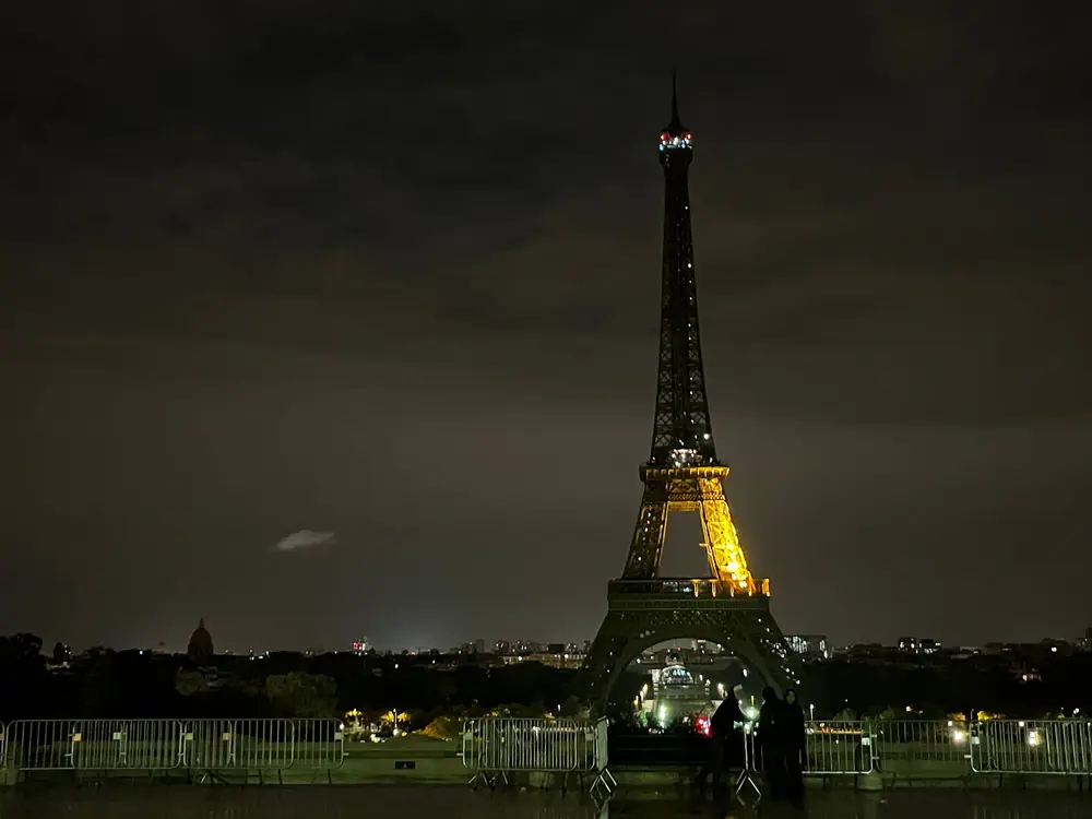 The illuminated Eiffel Tower rising above visitors at night.