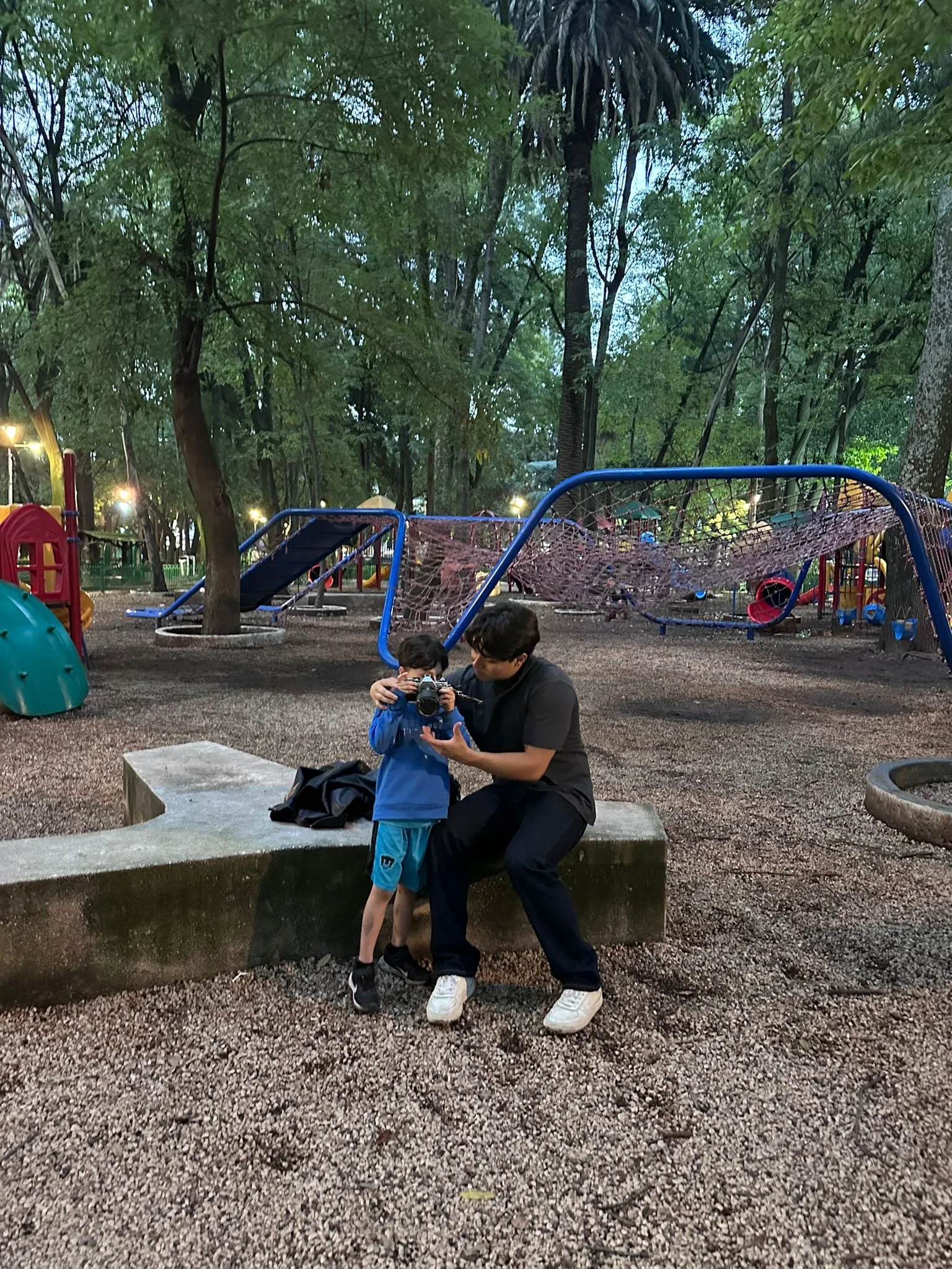 Two people seated beside a swing set in a shaded park.