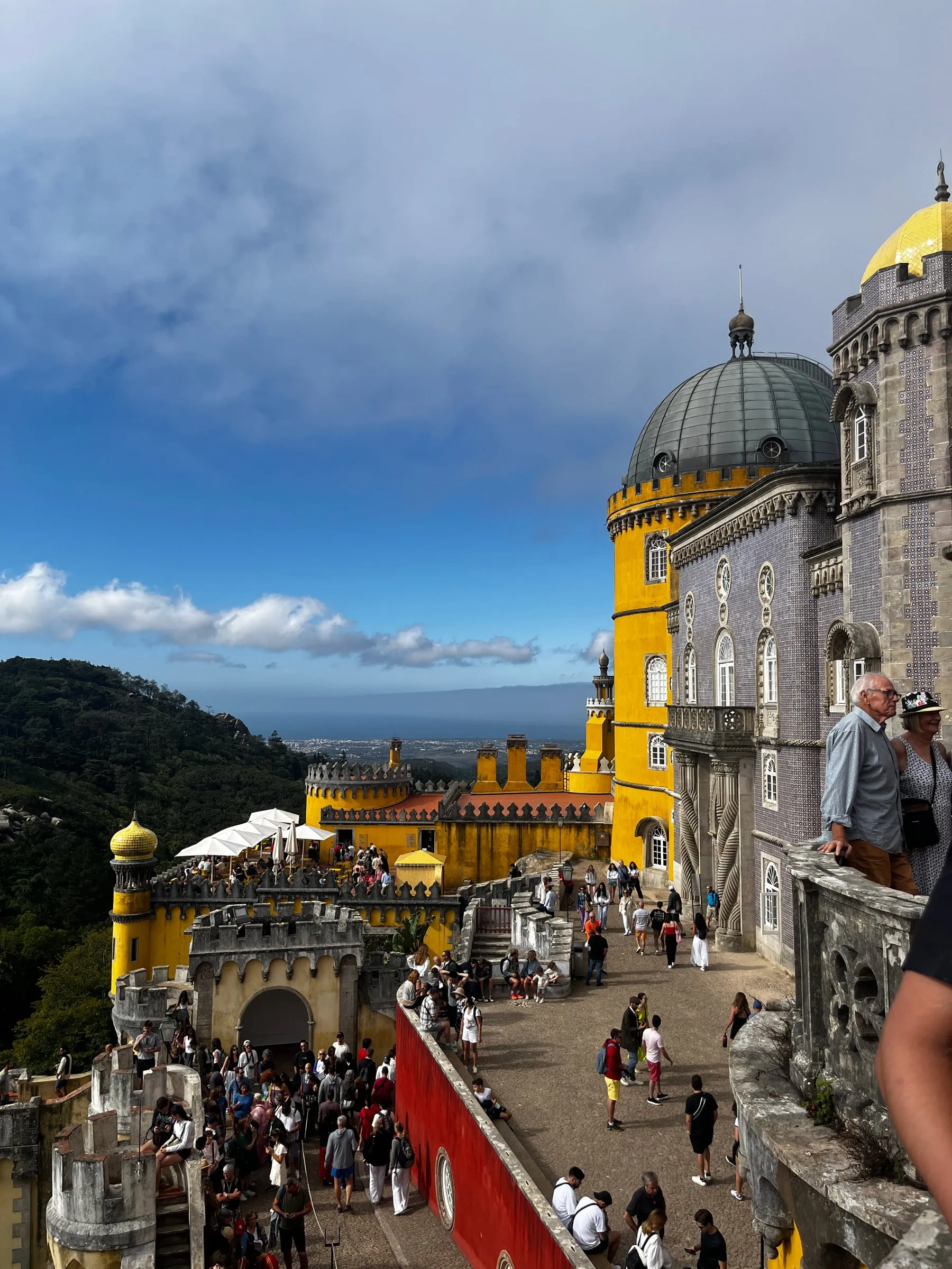 Visitors on terraces beside the yellow walls and domed towers of Pena Palace.