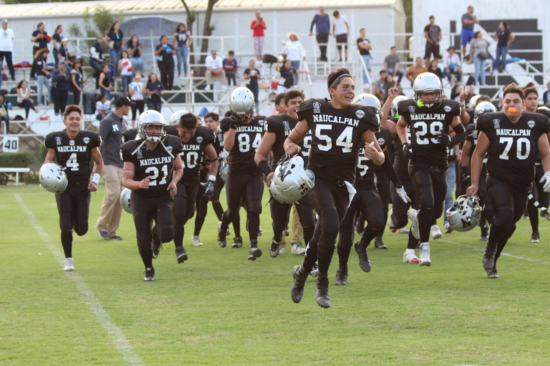An American football team in black uniforms running onto the field in front of spectators.